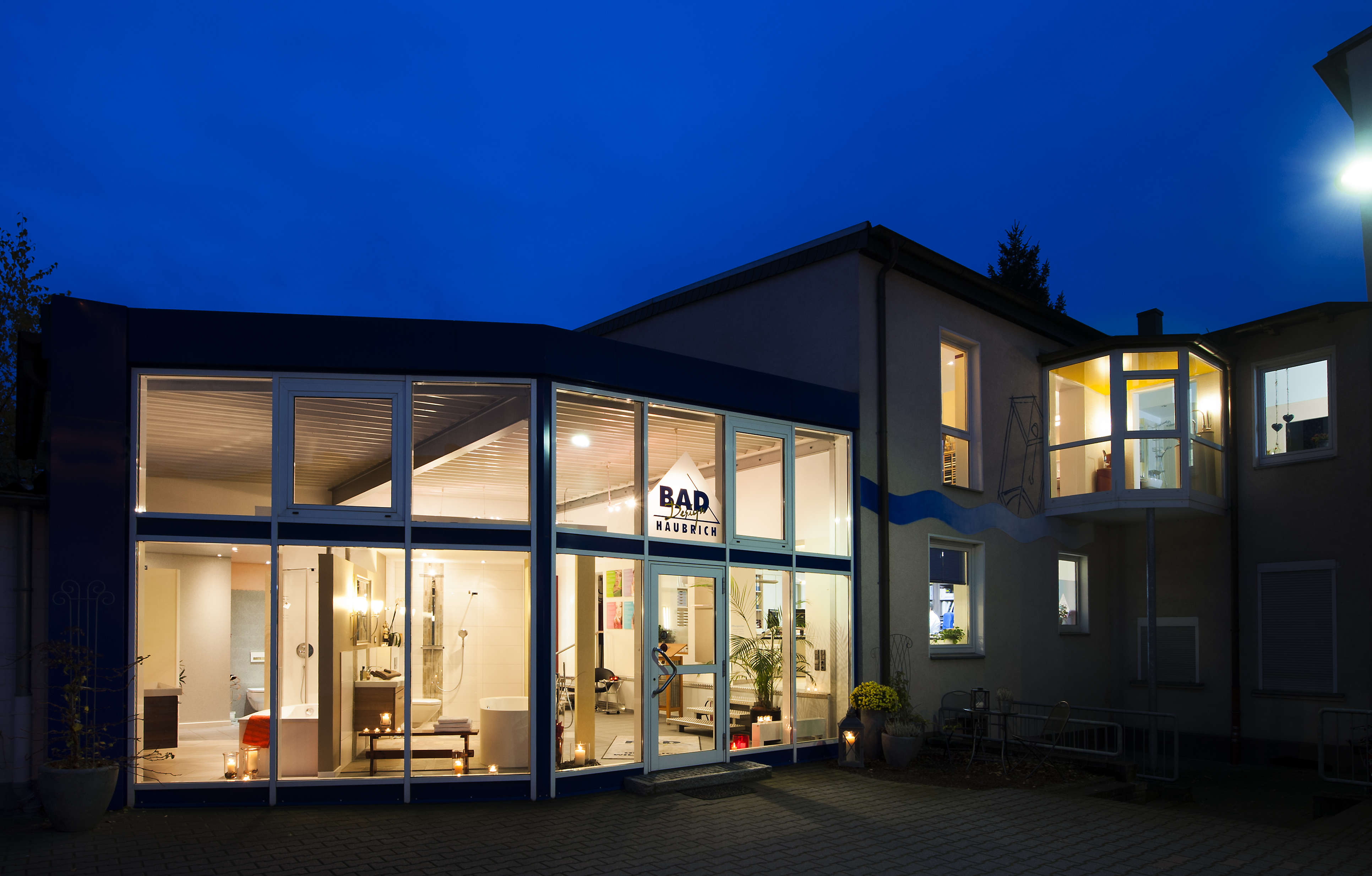 Eine Außenansicht des Badstudios von Haubrich Baddesign in Oberhausen. Ein zwei-stöckiges Gebäude mit einladender Beleuchtung.