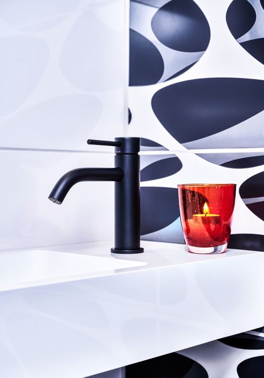 Zu sehen ist ein modernes Waschbecken mit schwarzem Wasserhahn. Daneben steht eine einladende Kerze für Atmosphäre.